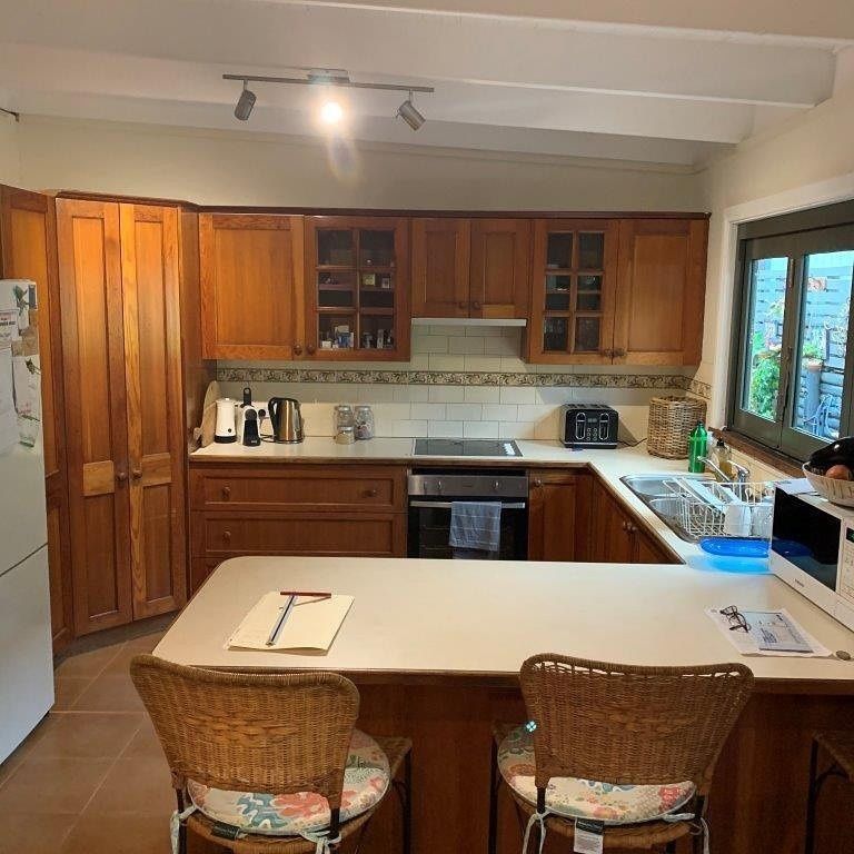 Kitchen with wooden cabinets, countertops, and two wicker bar stools — The Kitchen Centre In Tuggerah, NSW
