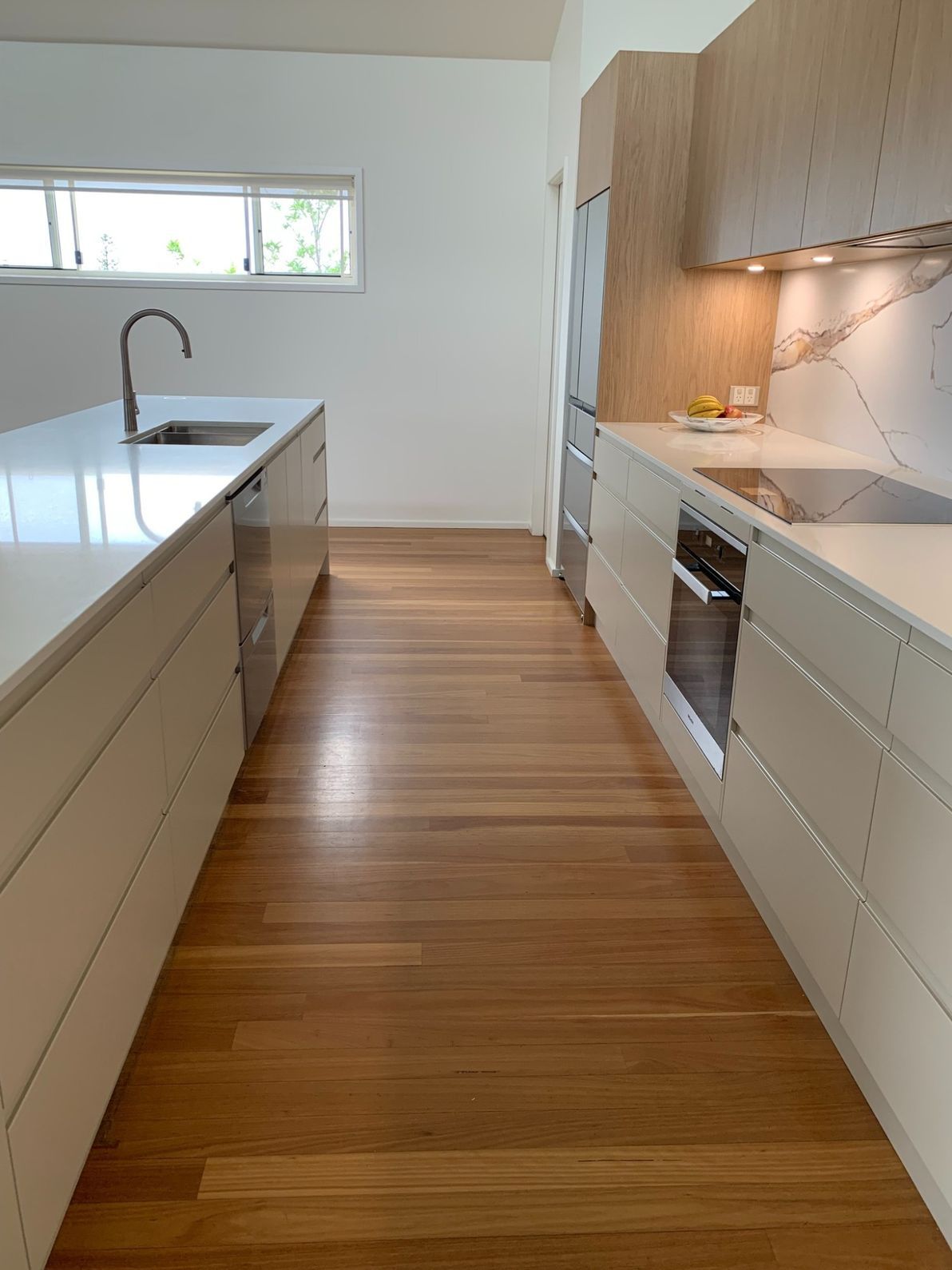 A Long Kitchen With White Cabinets and Wooden Floors — The Kitchen Centre In Tuggerah, NSW