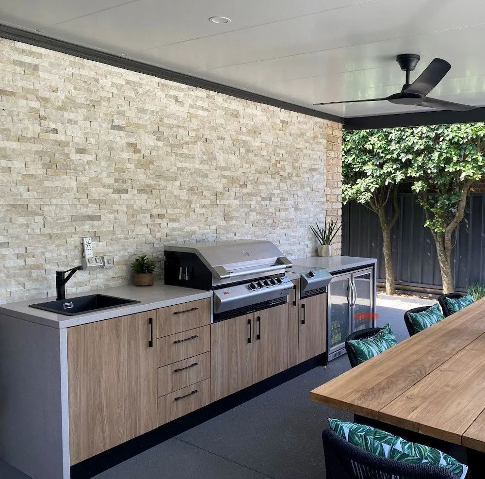 Outdoor Kitchen With Grill, Sink, and Cabinets Against a Stone Wall — The Kitchen Centre In Tuggerah, NSW