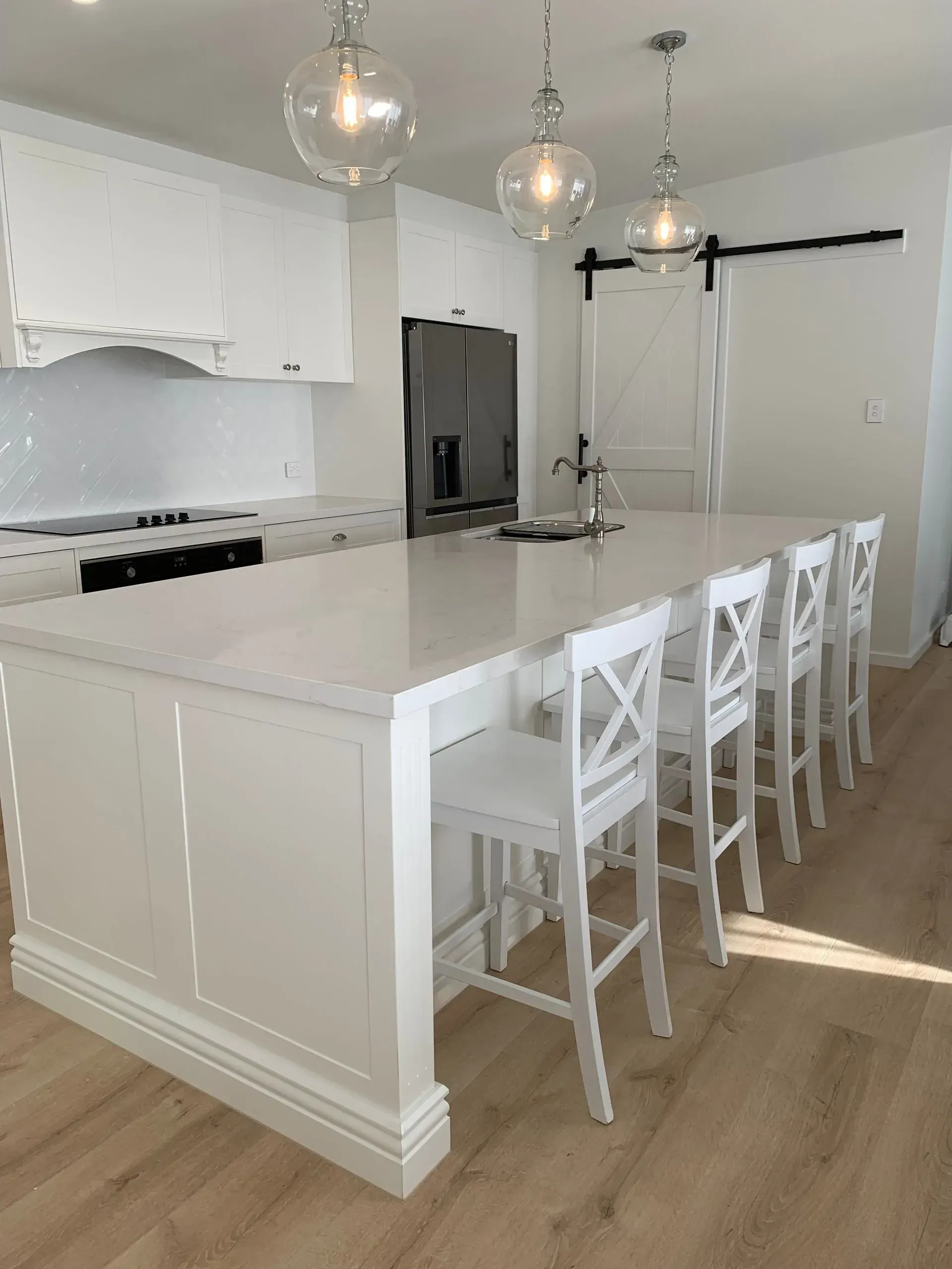 White Kitchen With Island, Bar Stools, Pendant Lights, and a Sliding Barn Door — The Kitchen Centre In Tuggerah, NSW