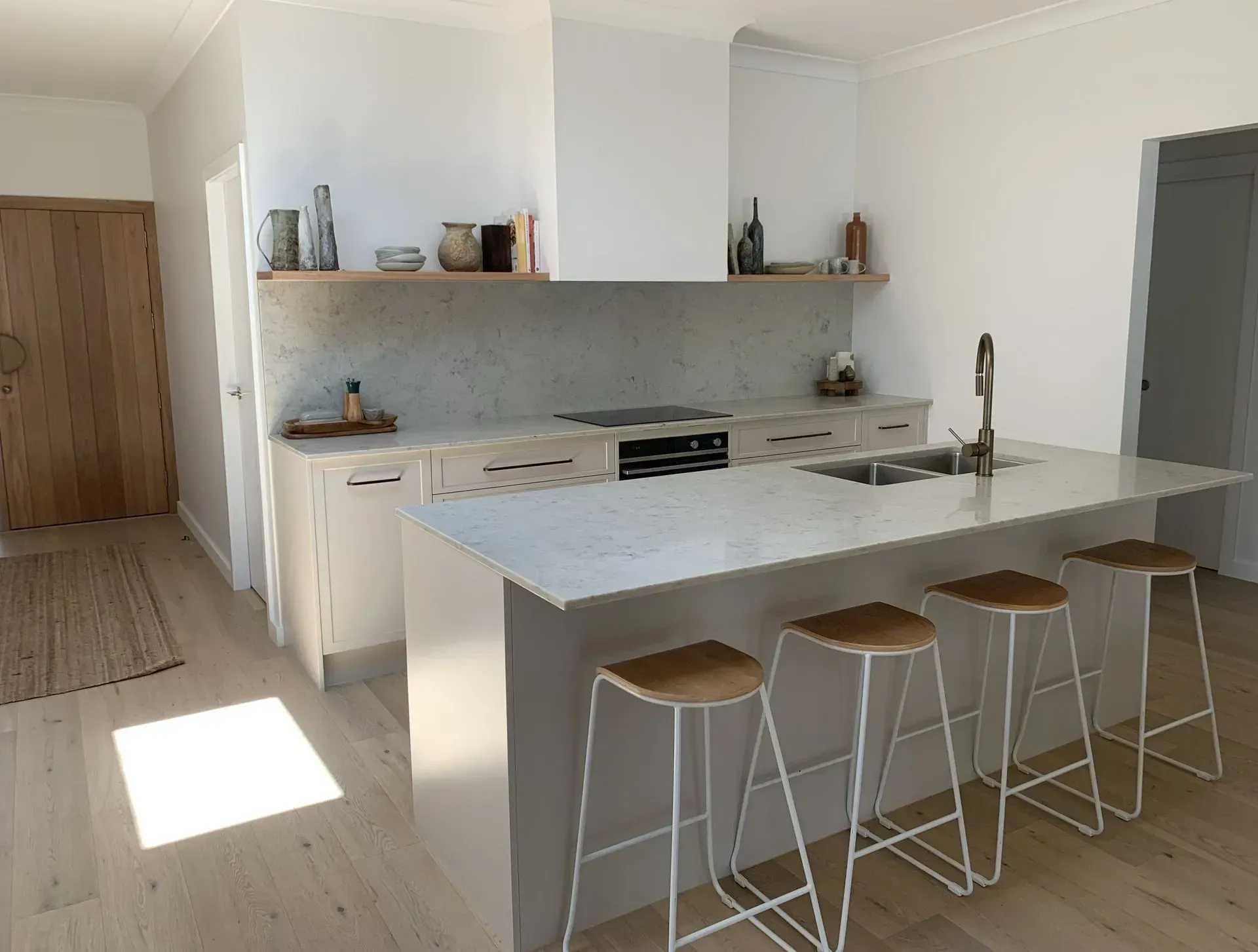 Modern White Kitchen With Island, Stools, and Wooden Door — The Kitchen Centre In Tuggerah, NSW