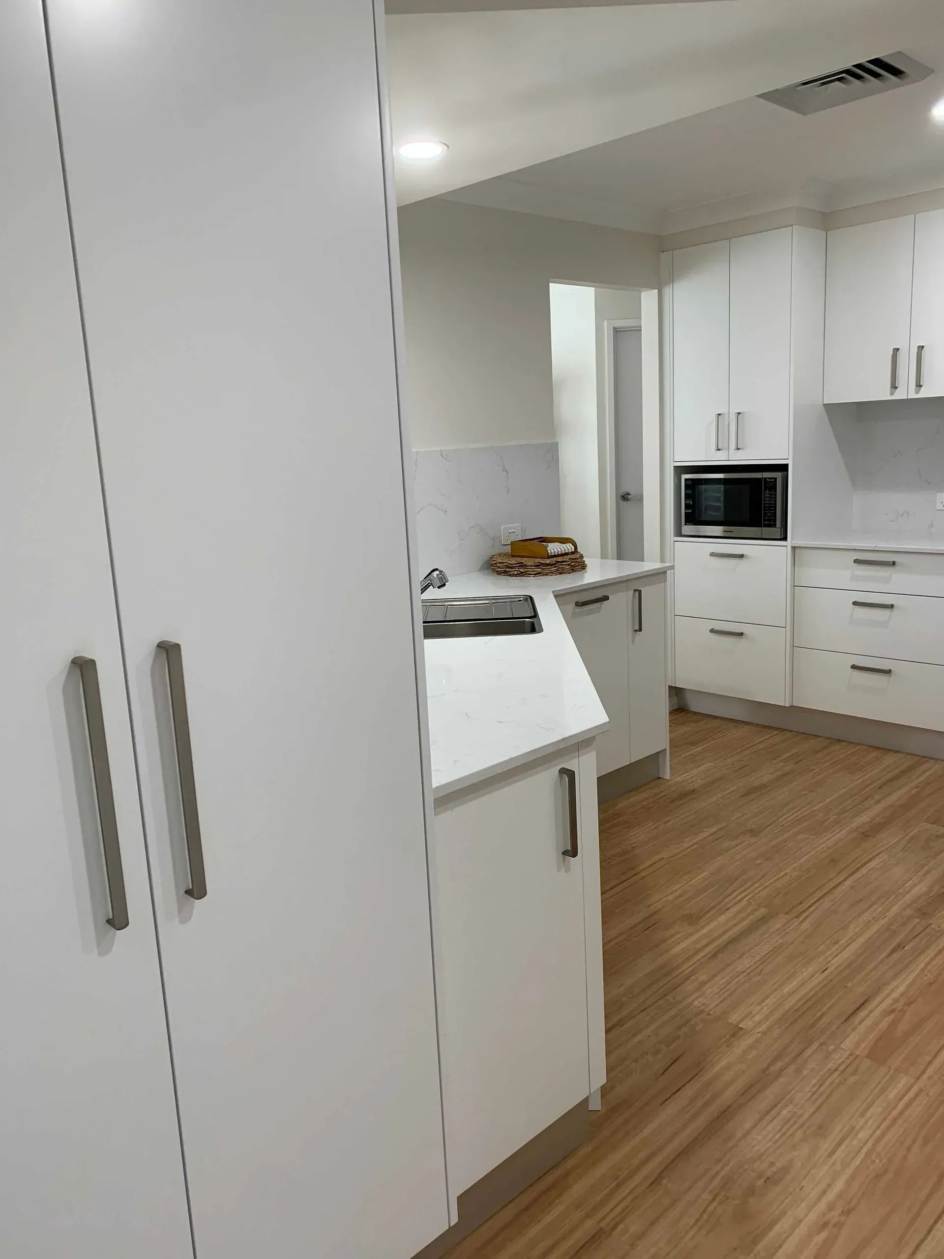White Kitchen With White Cabinets, Quartz Countertops, and Wood-look Flooring — The Kitchen Centre In Tuggerah, NSW