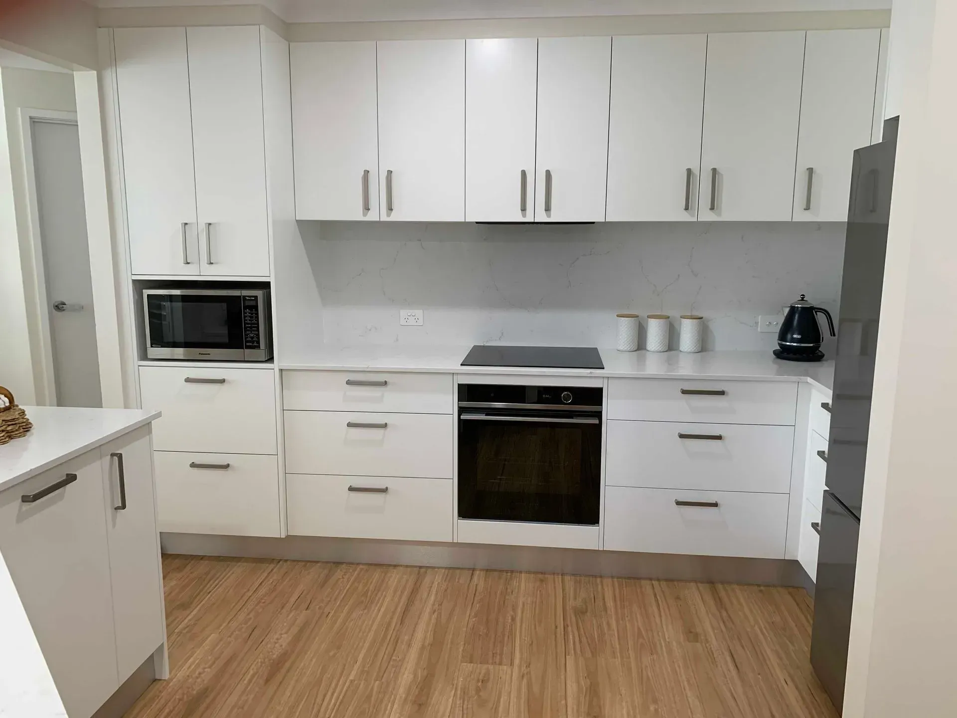 White Kitchen With Upper and Lower Cabinets, Microwave, Oven, Cooktop, and Wooden Floor — The Kitchen Centre In Tuggerah, NSW