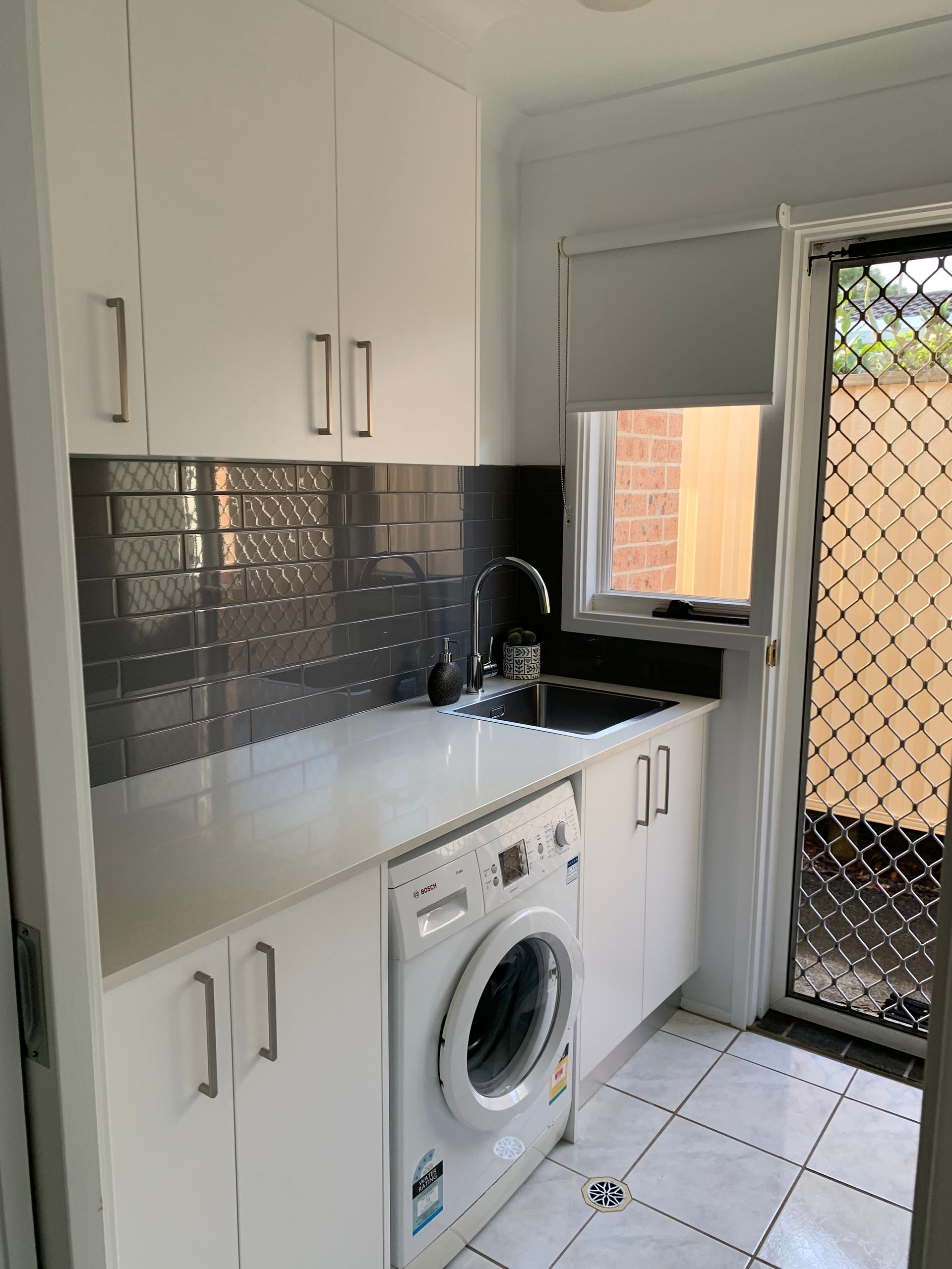 A Laundry Room With A Washing Machine, White Cabinets, and A Black Screen Door — The Kitchen Centre In Tuggerah, NSW