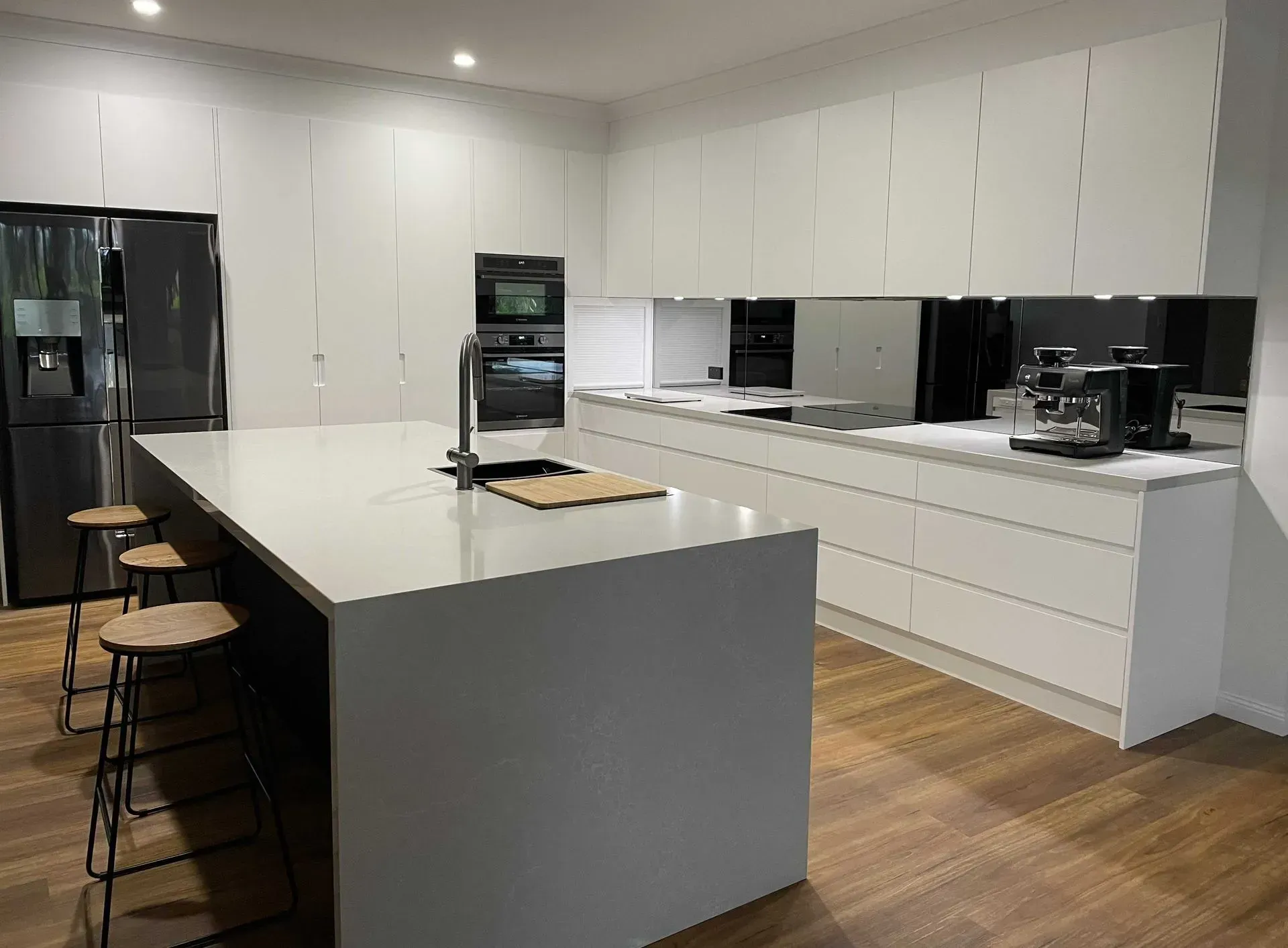 Modern White Kitchen With Large Island, Stools, and Stainless Steel Appliances — The Kitchen Centre In Tuggerah, NSW