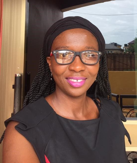 Woman wearing glasses and a black headwrap, smiling, wearing a black top.