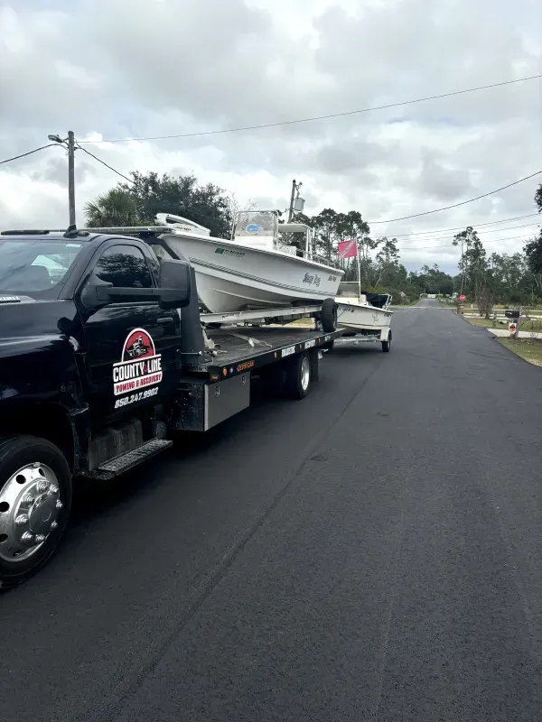 A tow truck is carrying a boat down a street.
