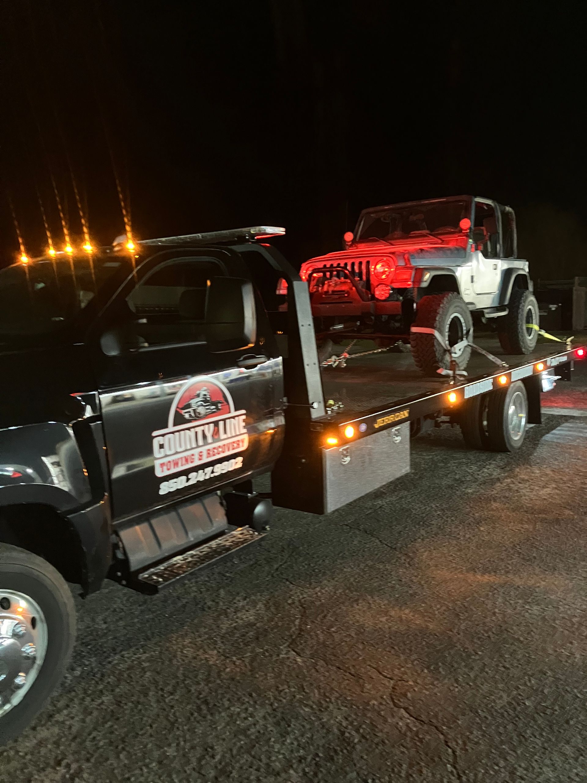 Tow truck with a white Jeep on its flatbed at night.