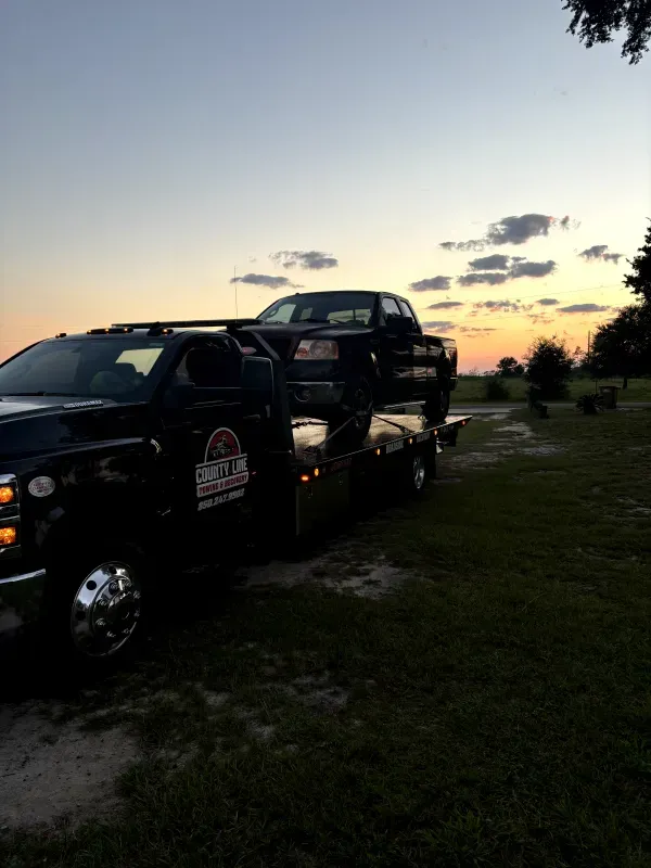 A tow truck is towing a car in a field at sunset.