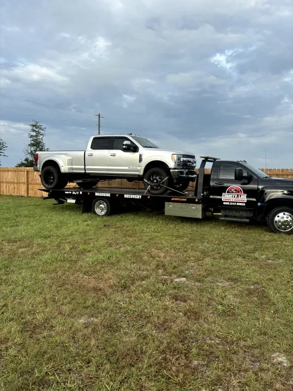 A white truck is being towed by a tow truck in a field.