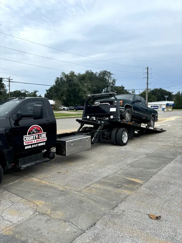 A tow truck is towing a black truck in a parking lot.