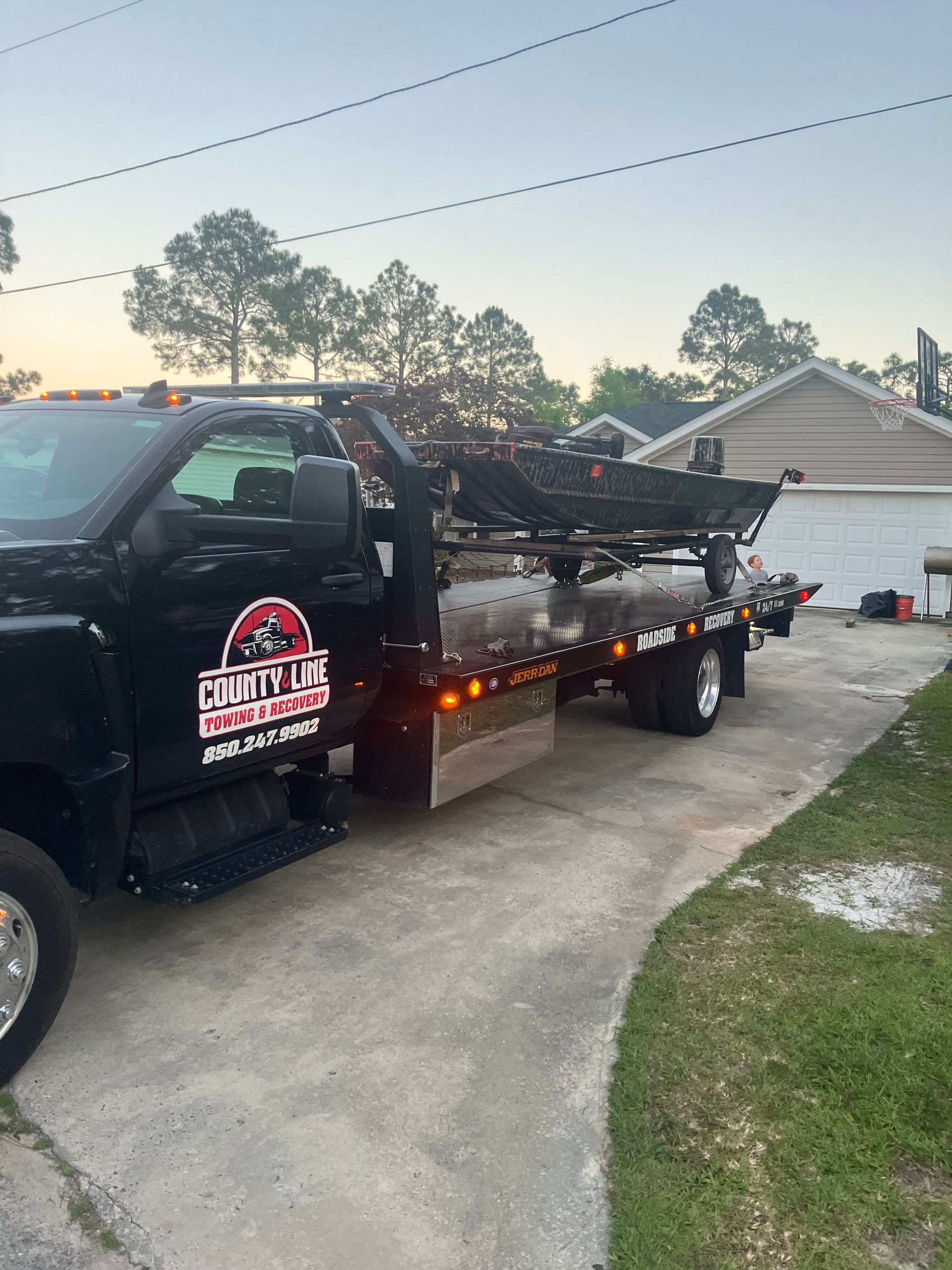 Black tow truck parked in a driveway, ready to tow a vehicle. The truck has a company logo.