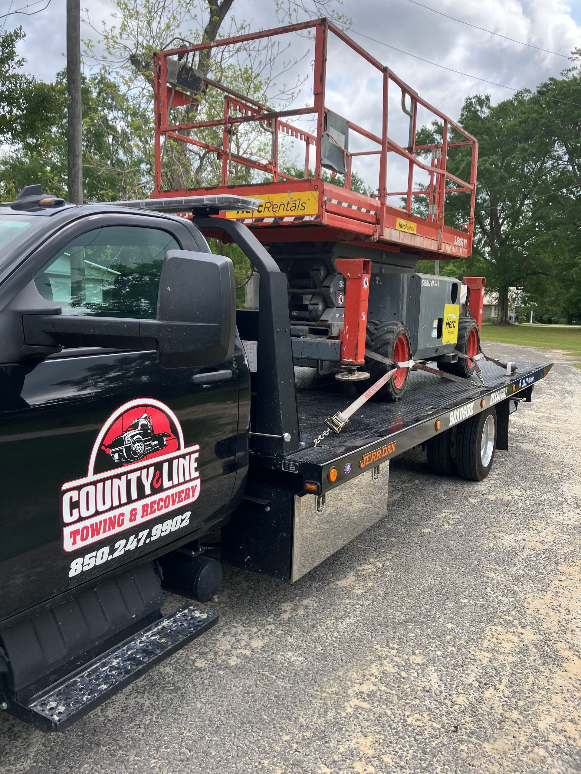 Black truck with County Line Towing & Repair logo, carrying a red scissor lift.