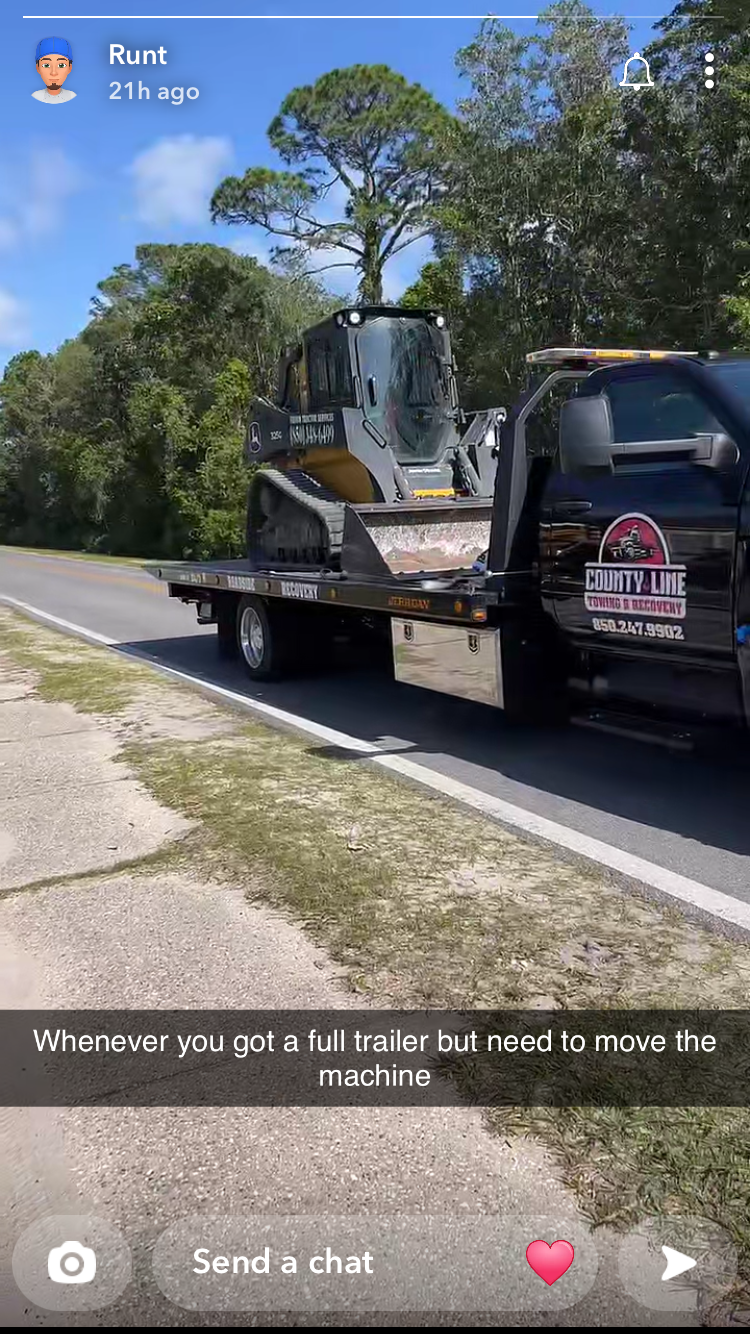 Skid steer loader on a flatbed truck; roadside setting.