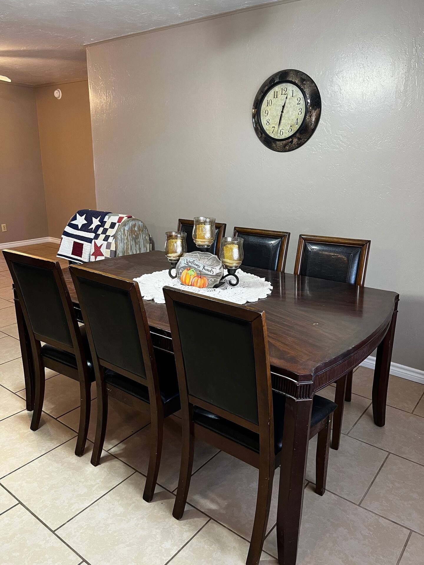 A dining room with a table and chairs and a clock on the wall.