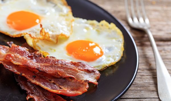 A plate of eggs and bacon with a fork on a wooden table.