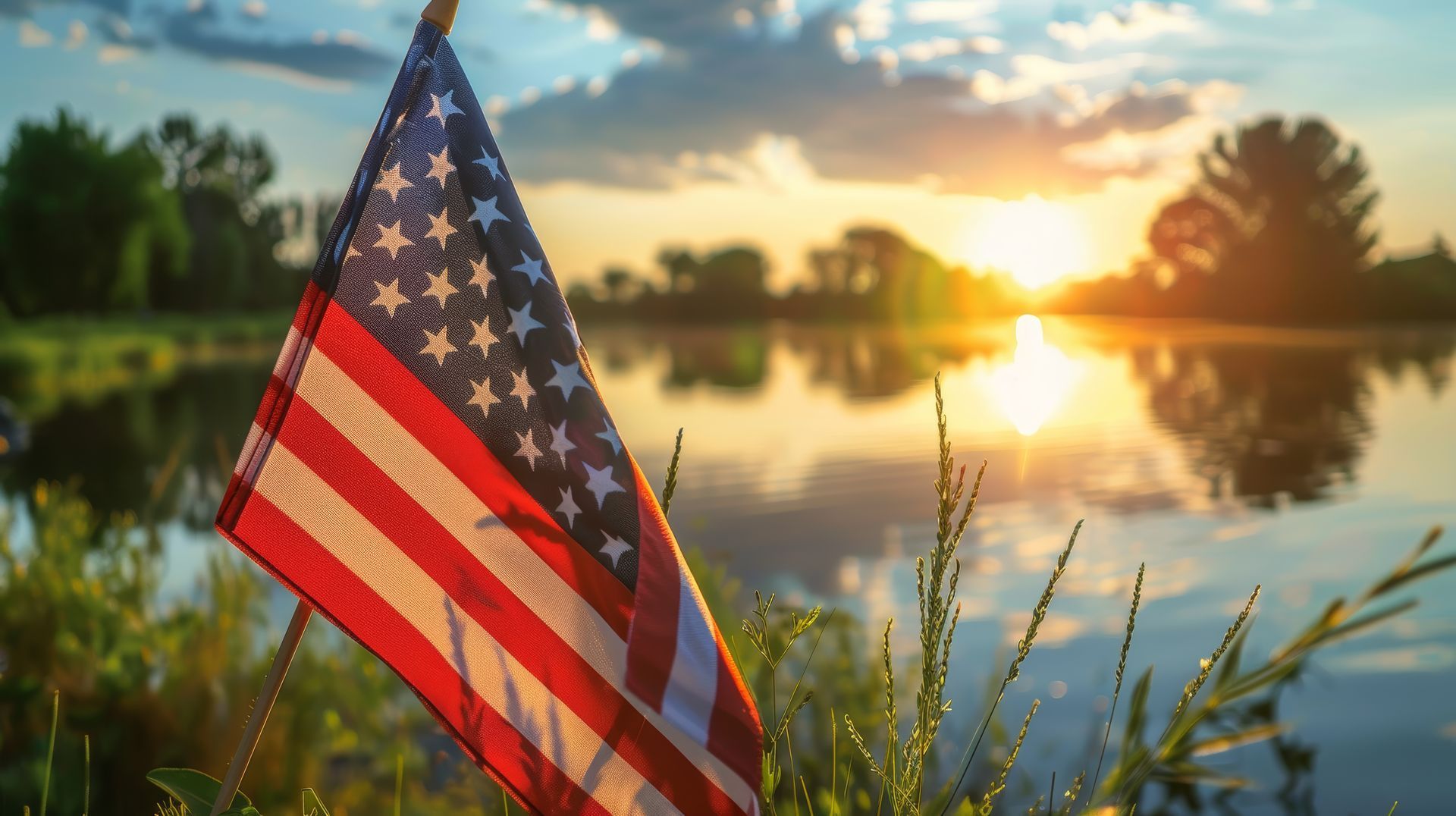 An american flag is sitting in the grass near a lake at sunset.