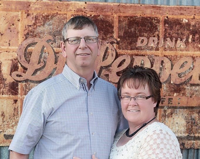 A man and a woman are posing for a picture in front of a rusty sign that says drink