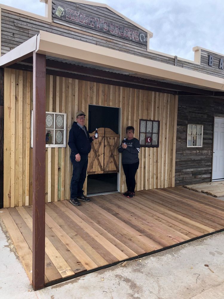 Two men are standing on a wooden deck in front of a wooden building.