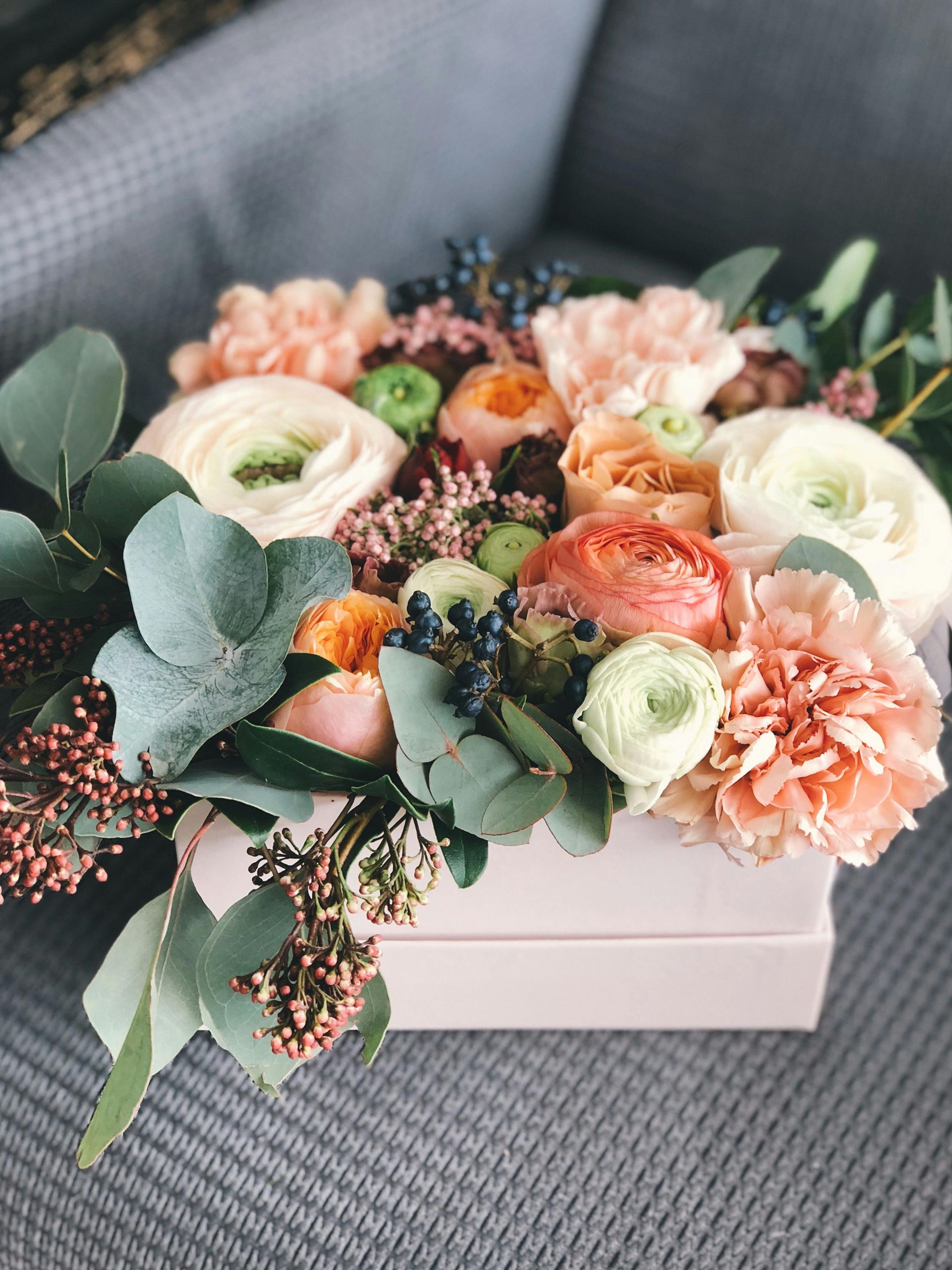 A box filled with flowers is sitting on a couch.