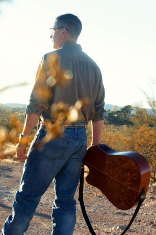 A man is holding a guitar in the desert