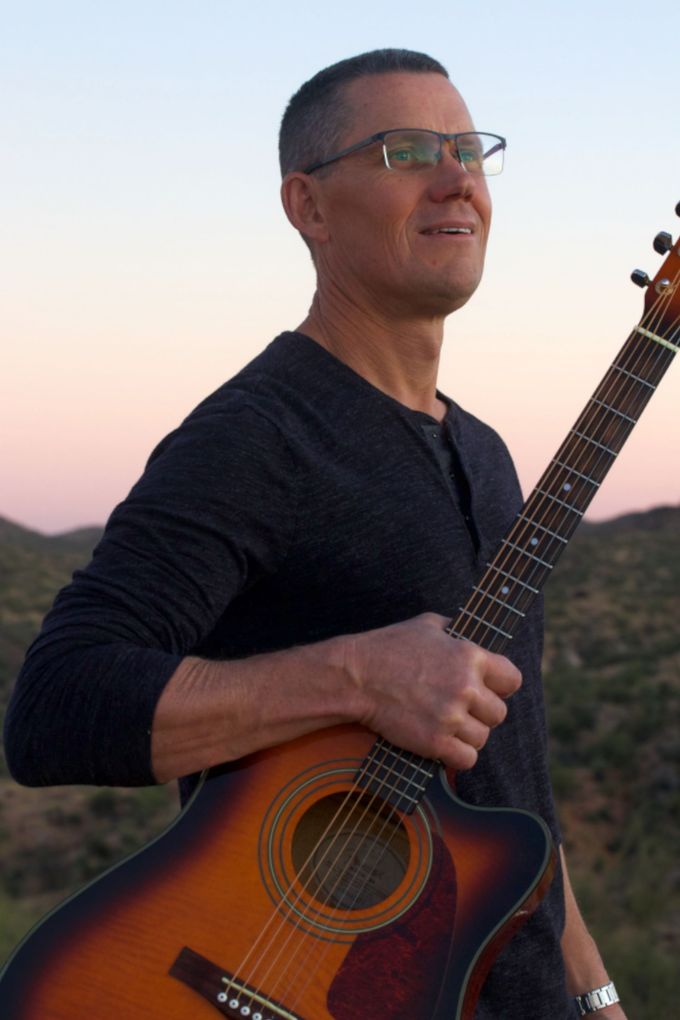 A man wearing glasses is holding an acoustic guitar