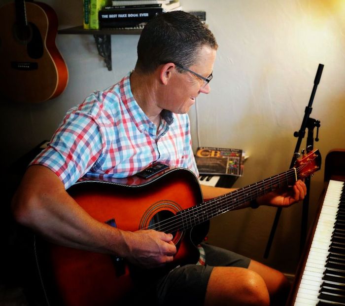 A man is playing an acoustic guitar next to a piano