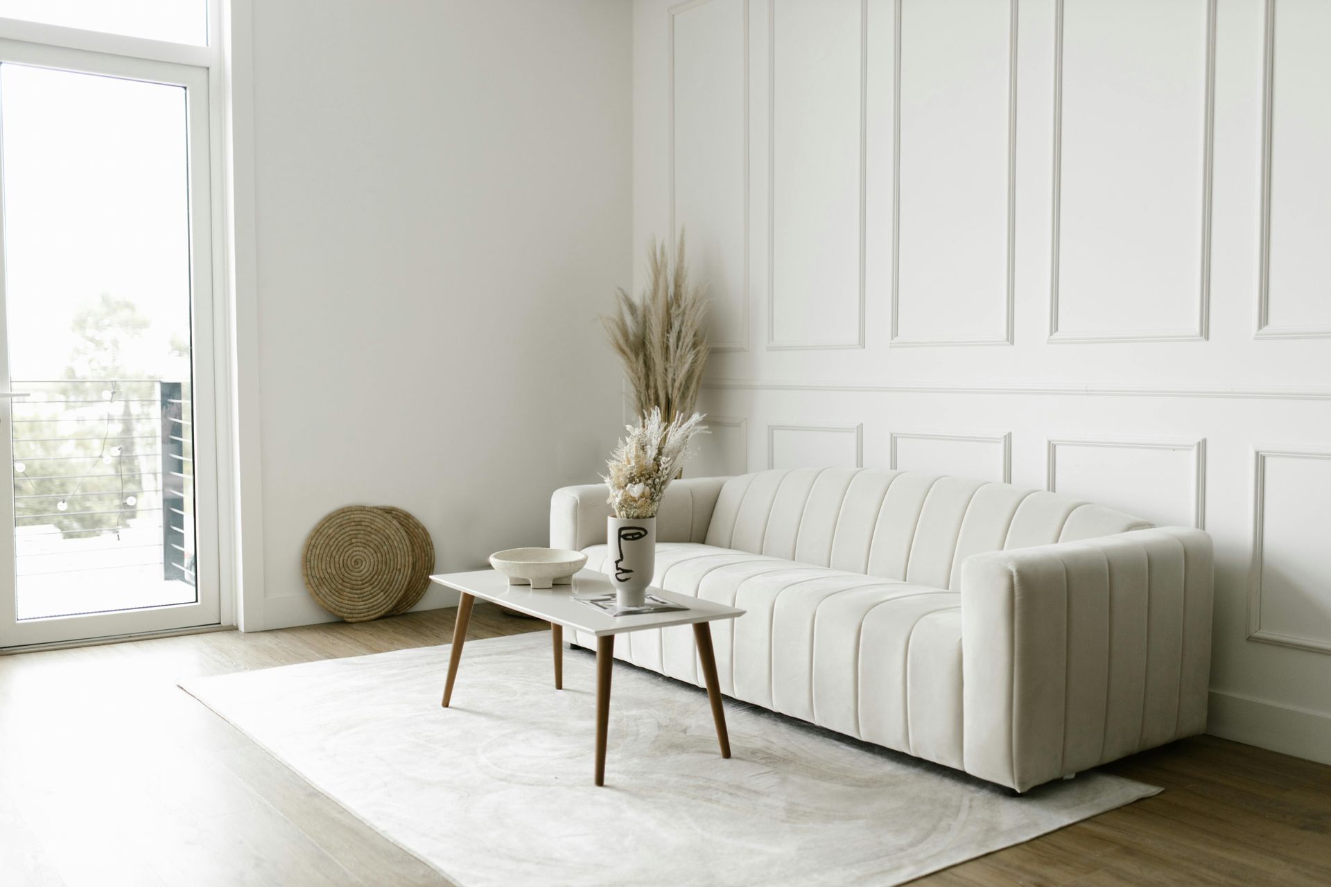 Cream-colored sofa in a minimalist living room with a coffee table, rug, and pampas grass decor.