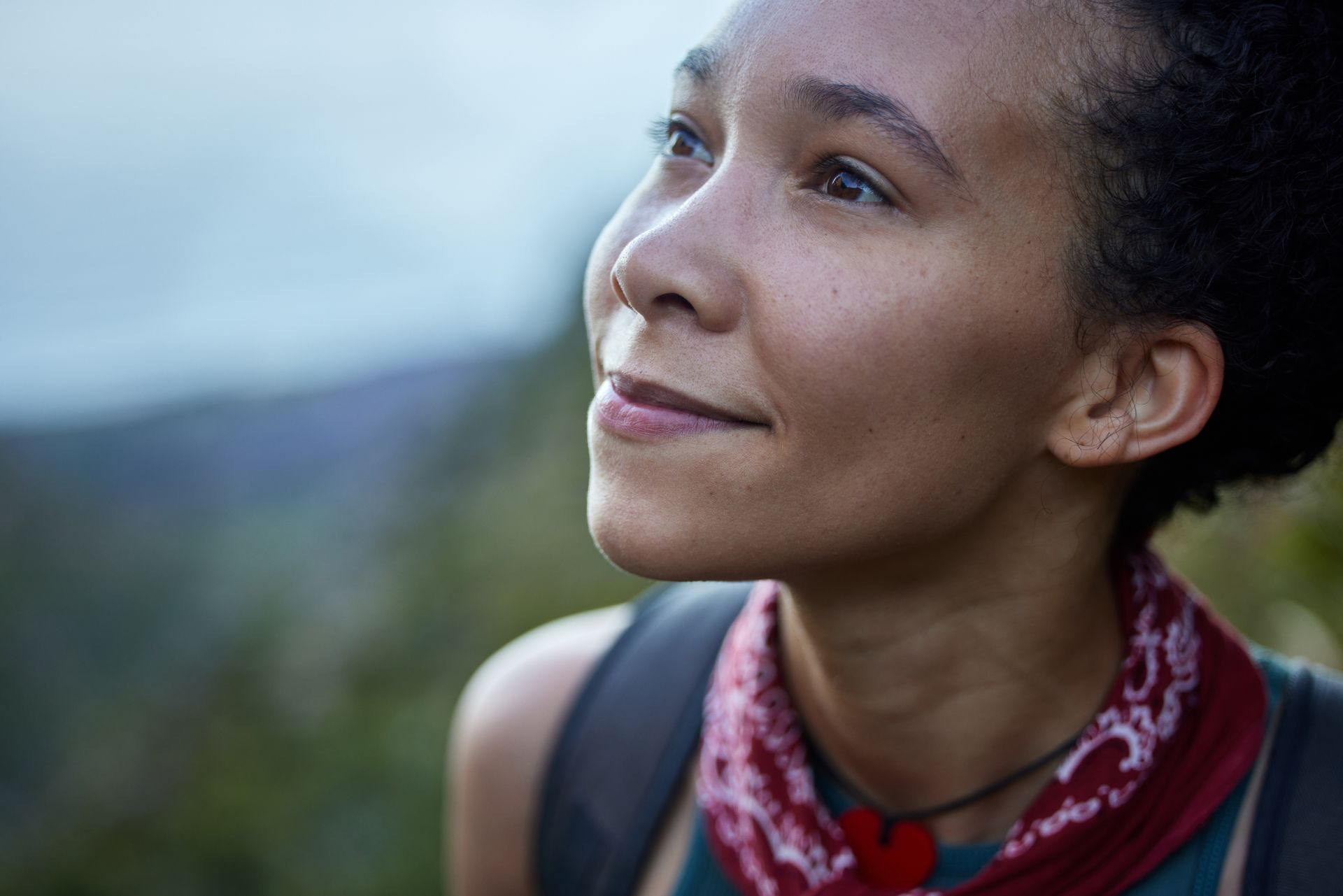 A person with a red patterned bandana gazes upward with a serene expression, outdoors in a soft-focus natural setting.