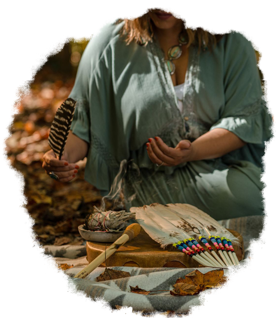Woman holding a feather, surrounded by ritual items: bowl, drum, fan. Soft light, outdoor setting.