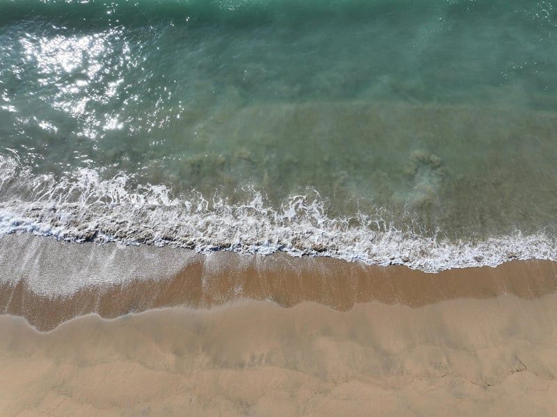 Aerial view of a sandy beach with turquoise ocean water and foamy waves washing ashore.