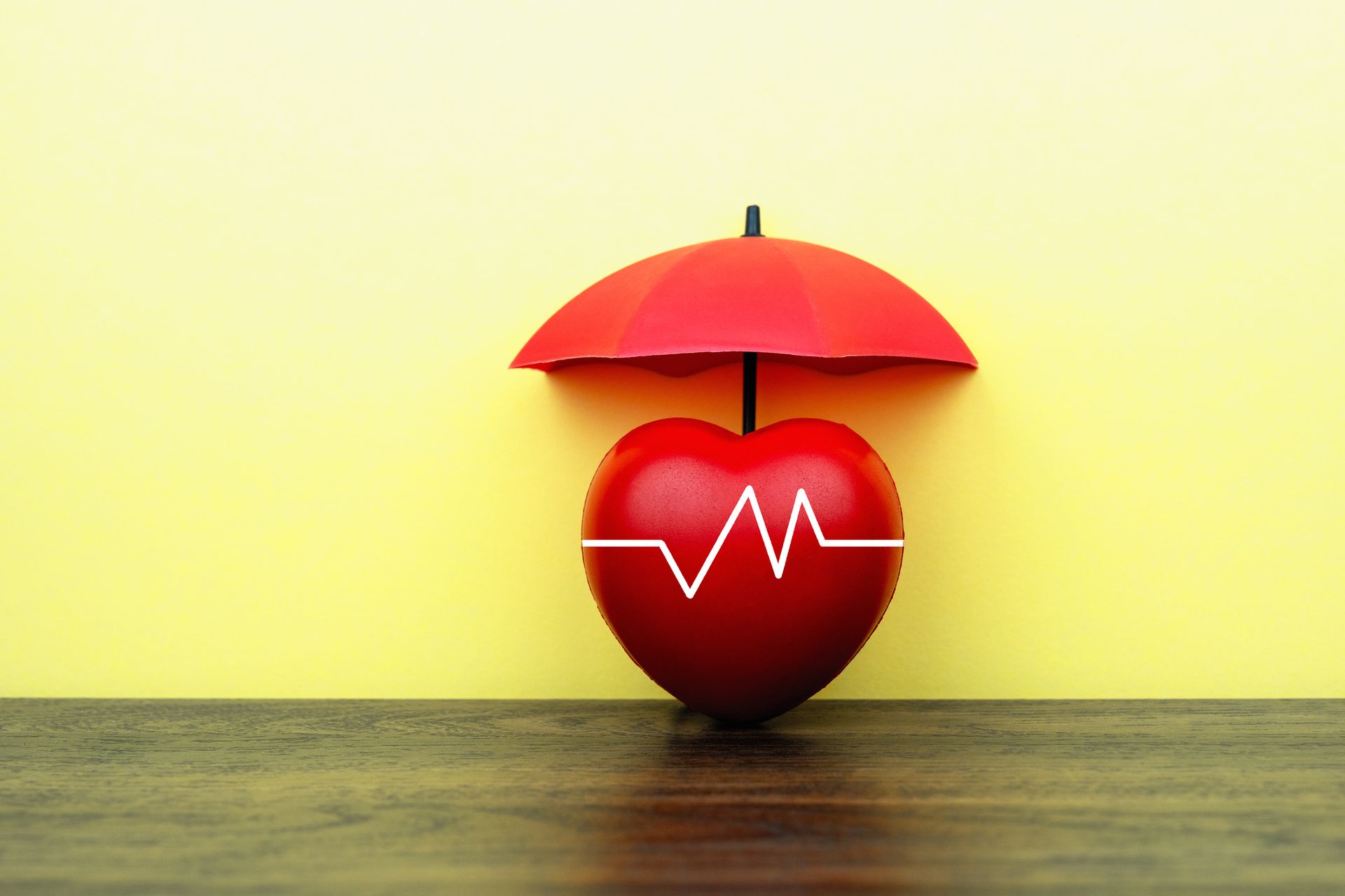 Red heart with heartbeat line under a red umbrella on a wooden surface against a yellow background.