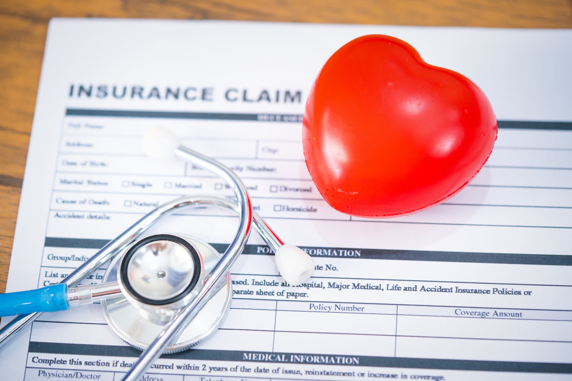 Insurance claim form, red heart, and stethoscope on a wooden surface.