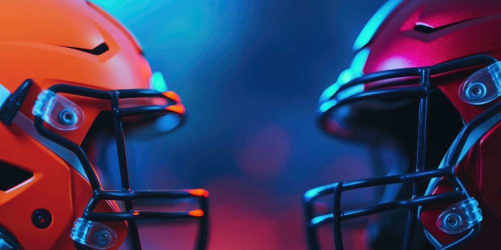 Two football helmets are facing each other in a dark room.