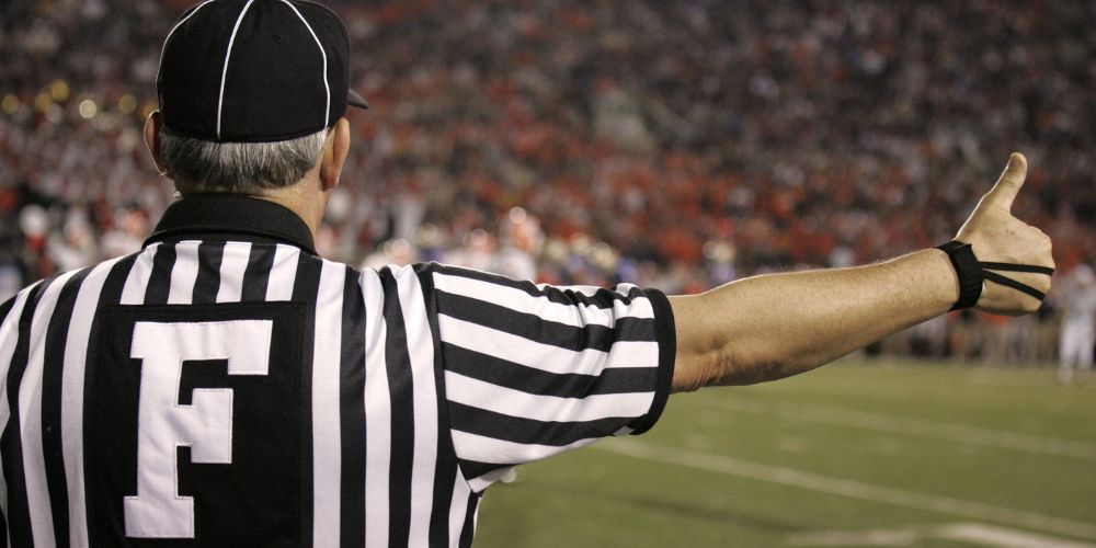 A referee is giving a thumbs up on a football field.
