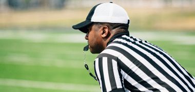 A referee is sitting on the sidelines of a football field.