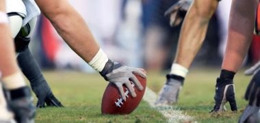 A football player is holding a football in his hand on a field.