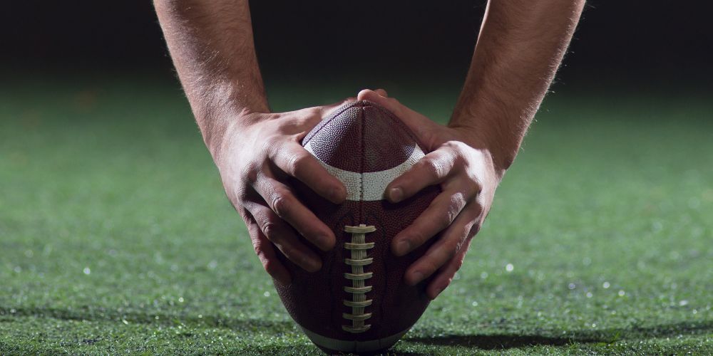 A person is holding a football in their hands on a field.