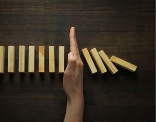A hand is pointing at a row of wooden blocks that are falling down.