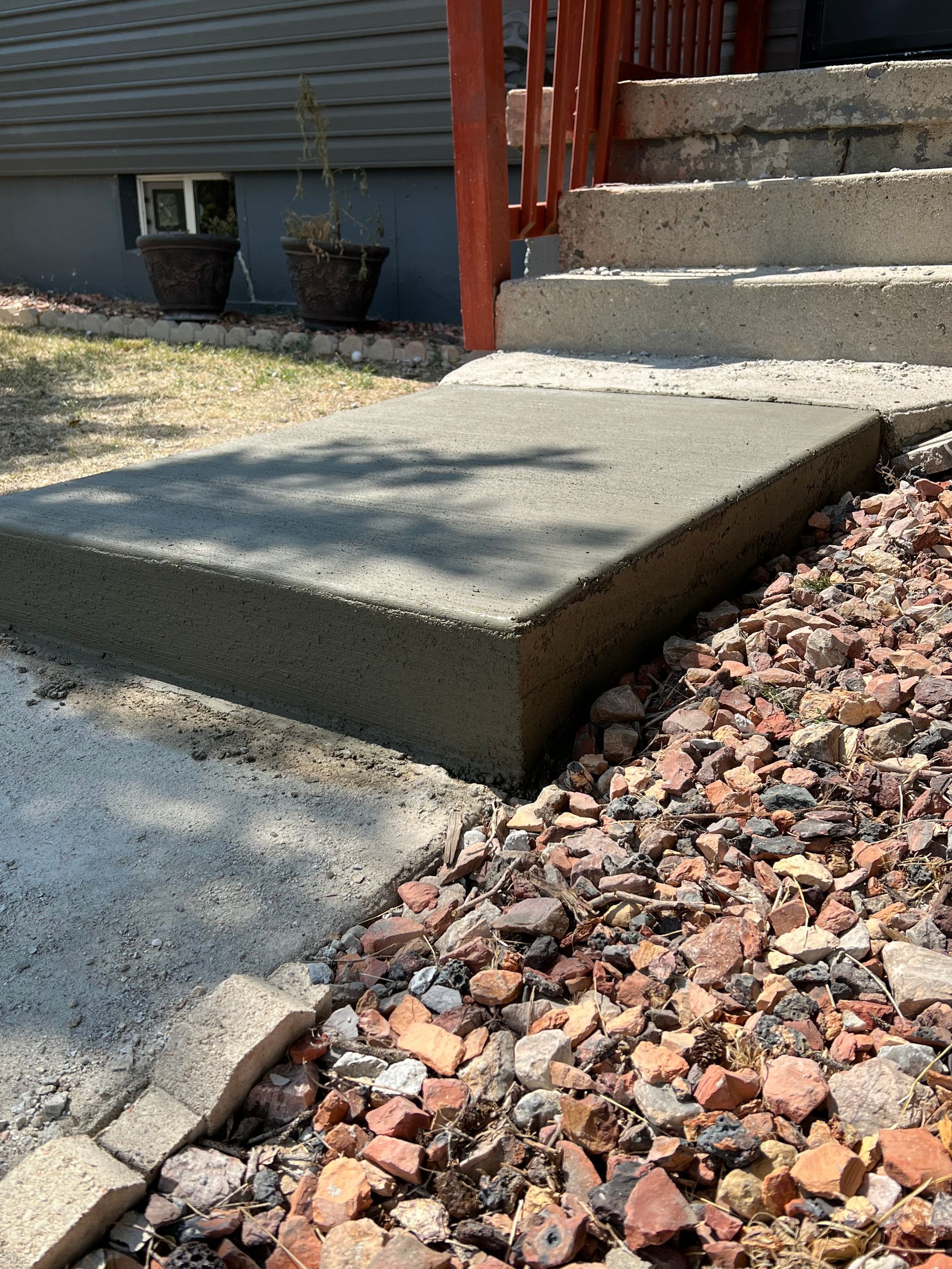 A concrete step leading up to a set of stairs next to a pile of gravel.