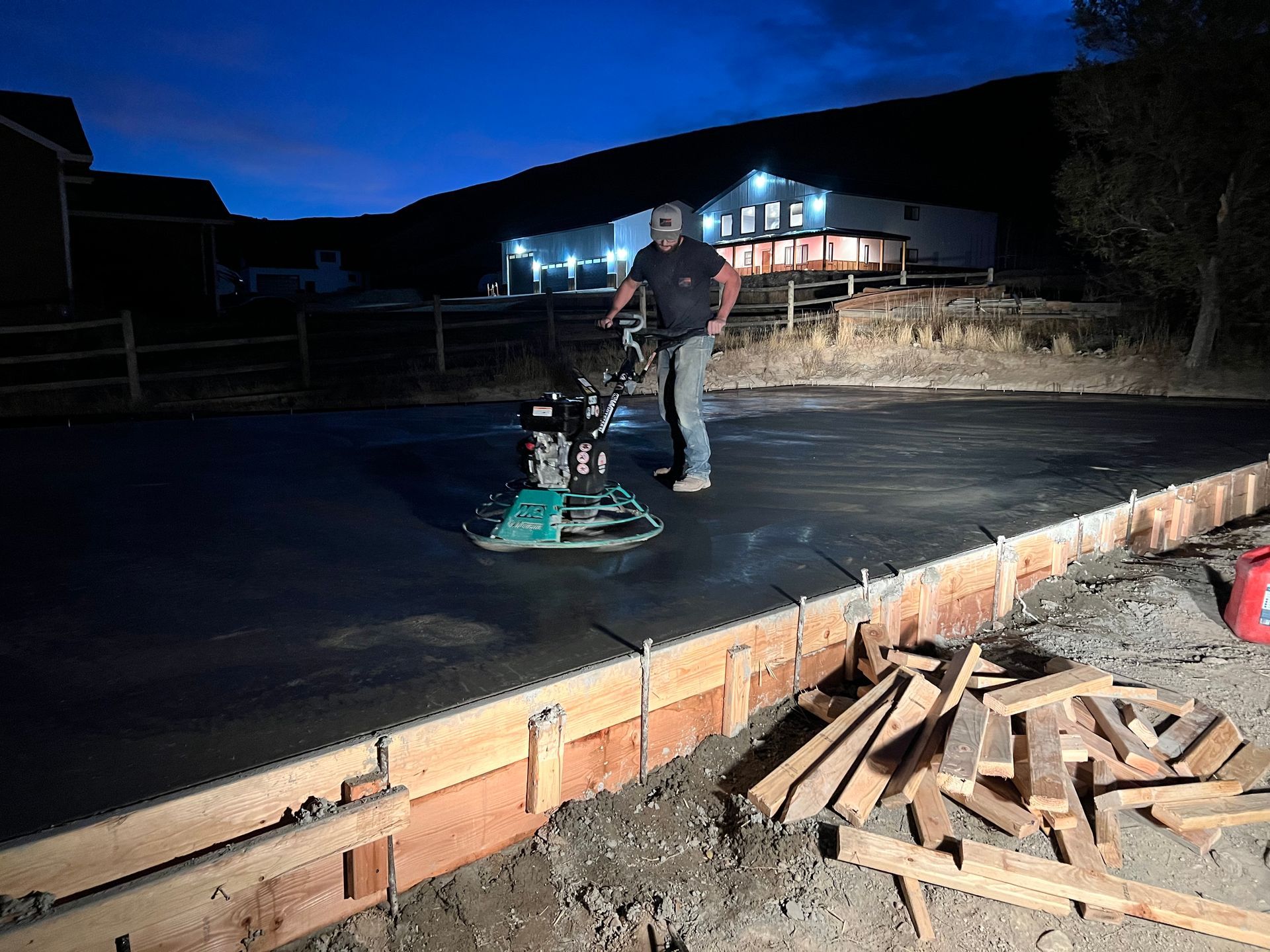 A man is working on a concrete driveway at night.