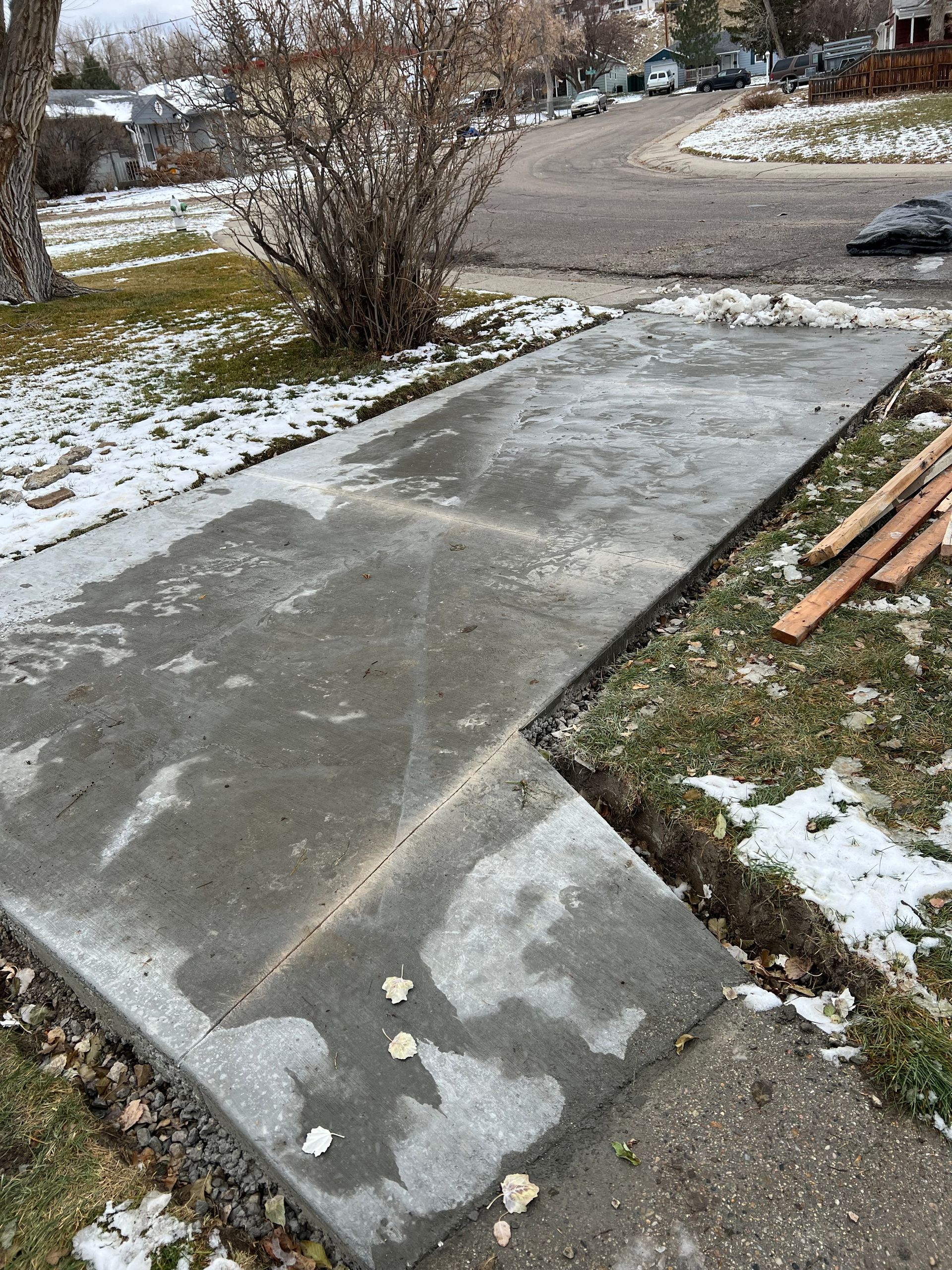 A concrete sidewalk is being built next to a snowy driveway.