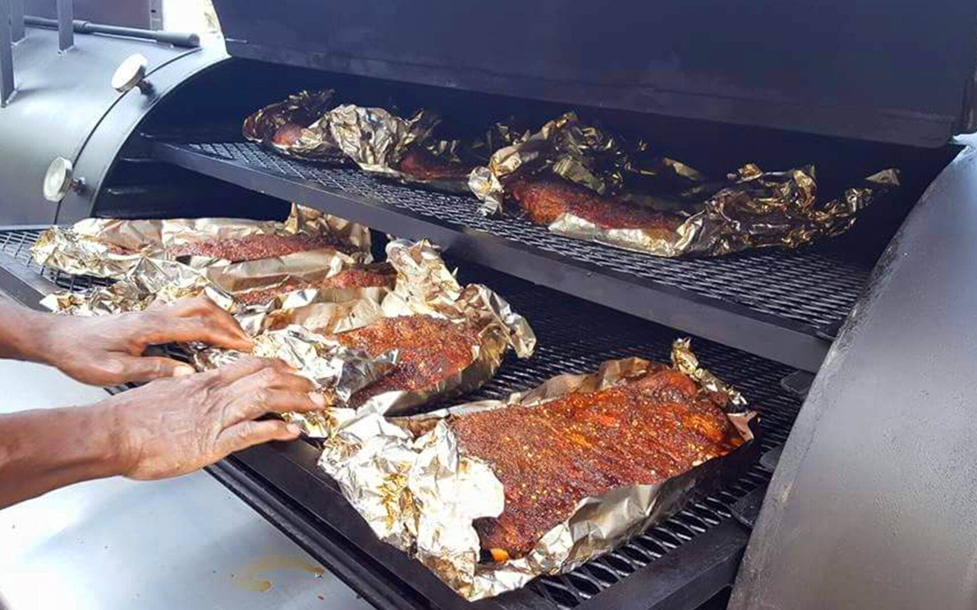A person is cooking meat on a grill with aluminum foil
