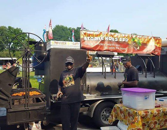 A man is standing in front of an atomic hogs bbq truck