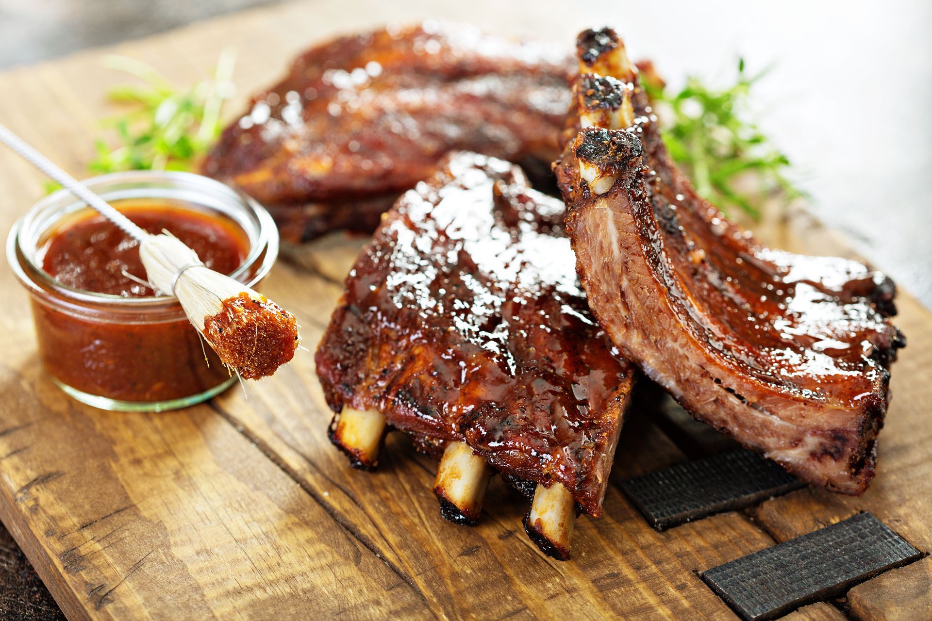 A wooden cutting board topped with ribs and a bowl of barbecue sauce
