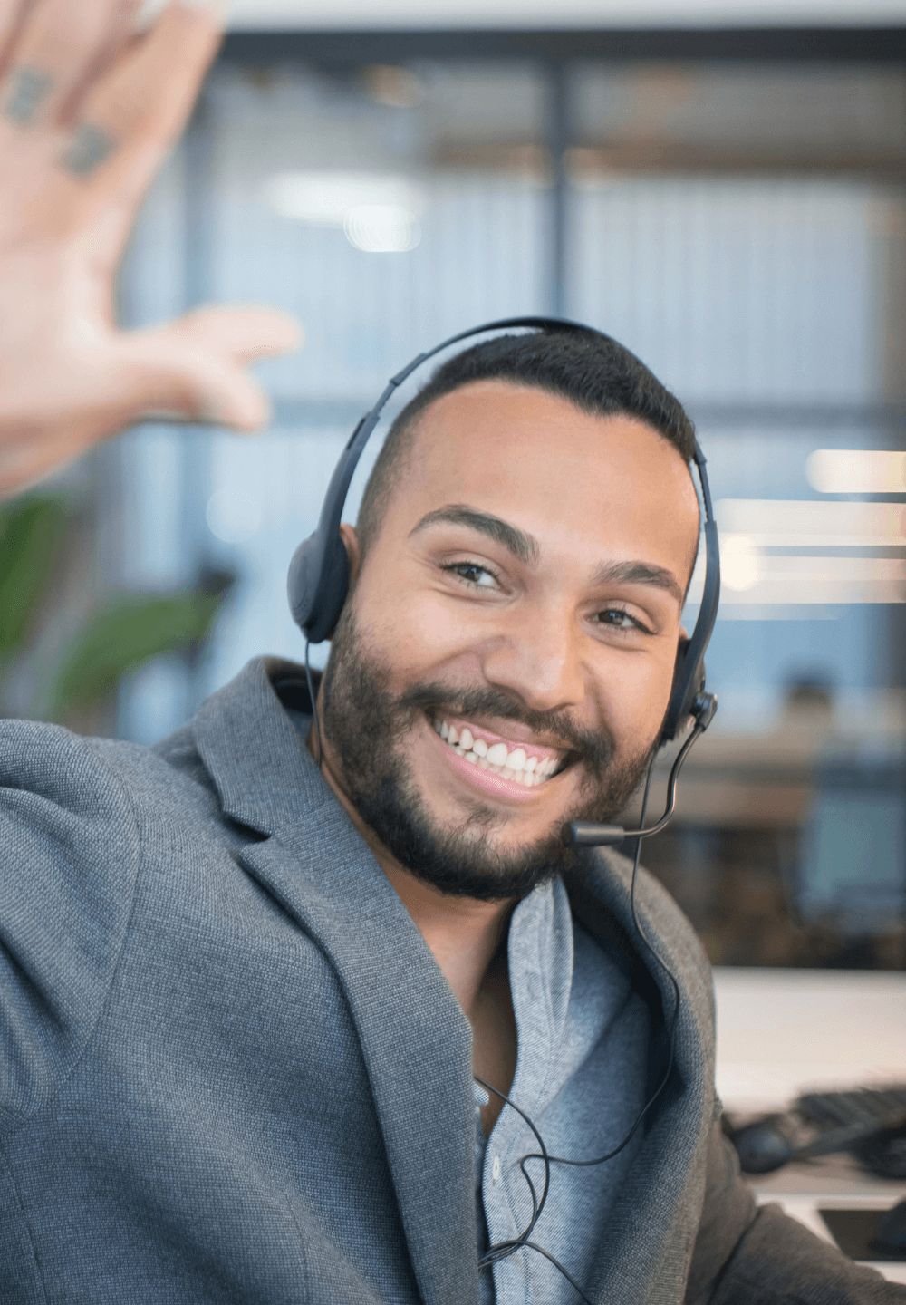 Een man met een headset glimlacht en zwaait in een kantooromgeving.