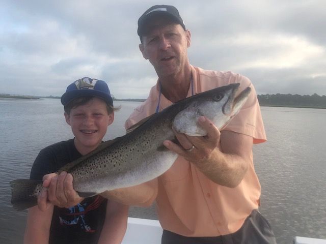 A man and a boy are holding a large fish on a boat.