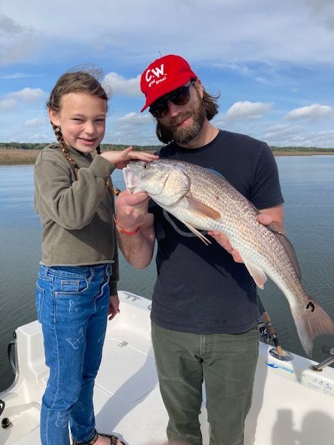A man and a little girl on a boat holding a large fish