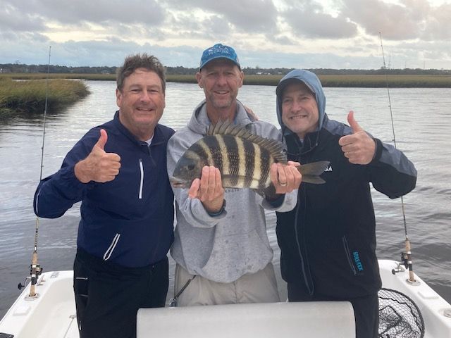 Three men on a boat holding a fish and giving a thumbs up