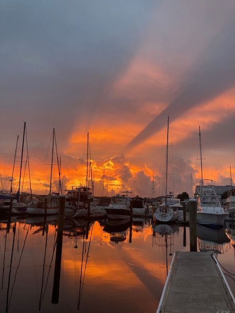 A sunset over a marina with boats docked and a dock in the foreground.